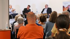 Blick auf die Diskussionsrunde aus dem Publikum. Auf dem Podium v.l.n.r Carlo Masala, Marc Mausch, Rüdiger Bachmann